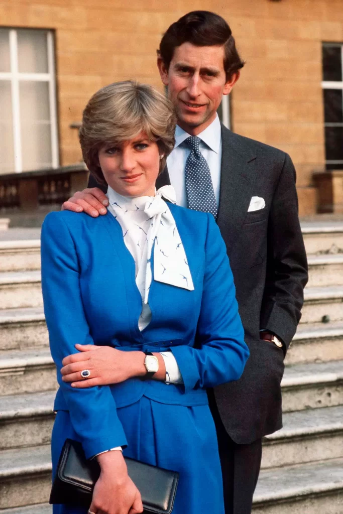 In questa foto Lady Diana e Carlo nel giorno dell'annuncio del fidanzamento. Lady Diana, in completo azzurro tiene la mano sinistra sul braccio destro e mostra il suo anello di fidanzamento con uno zaffiro blu circondato da diamanti