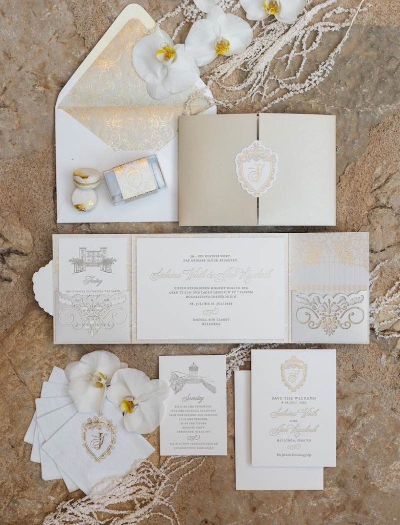 In questa foto un coordinato di matrimonio elegante colore dorato e bianco panna con logo degli sposi e font calligrafico