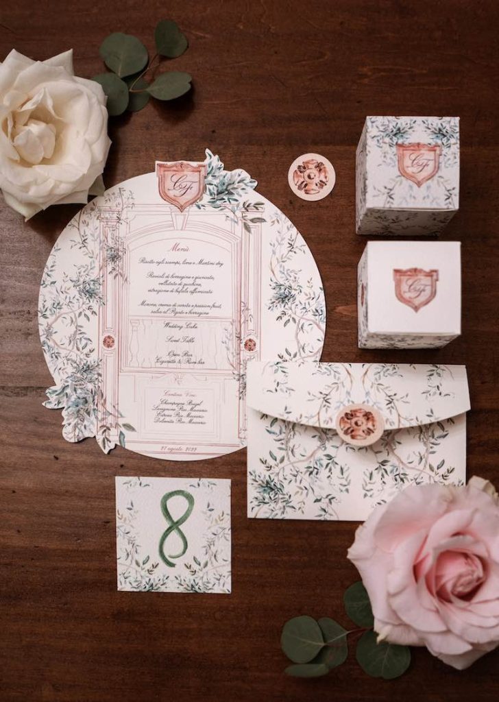 In questa foto un coordinato di matrimonio romantico con partecipazione su foglio rotondo, disegni di foglie verdi e dettagli di colore oro rosa