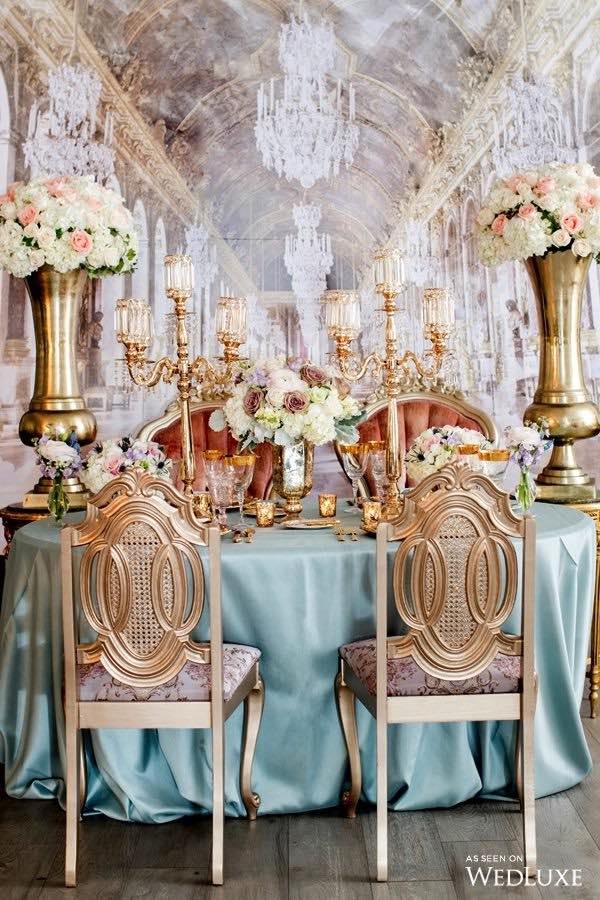 In questa foto un allestimento di matrimonio in stile Bridgerton con sedie di colore oro e velluto posizionato davanti ad un tavolo rotondo decorata con una tovaglia di colore verde acqua, candelabri e coppe di colore oro con fiori di colore bianco, rosa cipria e cappuccino