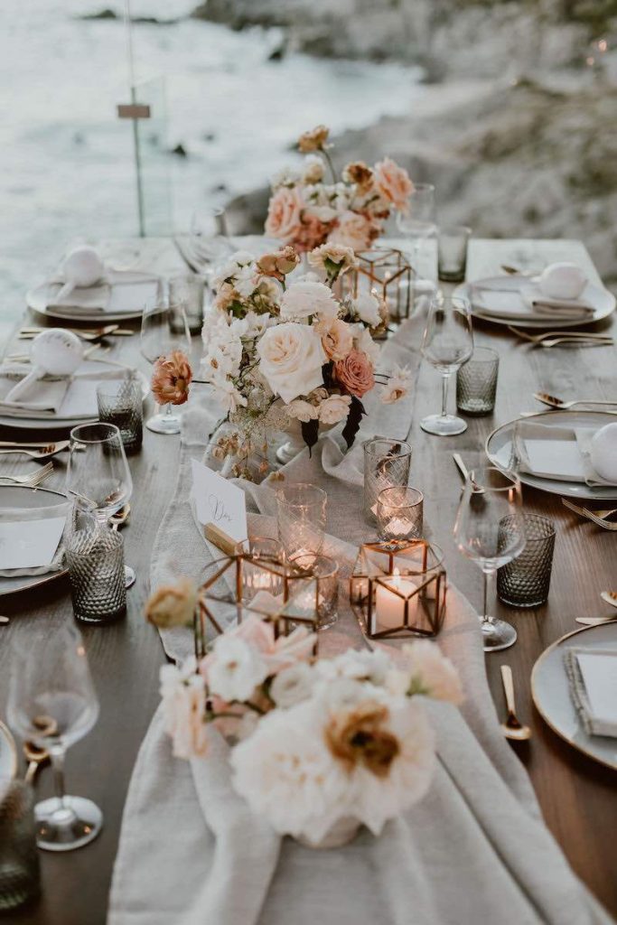 In questa foto un tavolo imperiale allestito per un matrimonio in stile boho chic con un runner di garza di colore verde salvia, rose di colore bianco e rosa e portacandele di vetro e metallo dorato