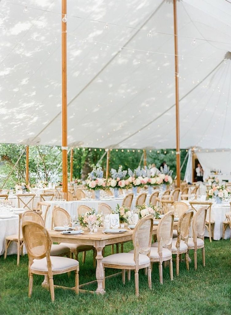 In questa foto un allestimento di matrimonio in stile classico su un prato con sedie e tavoli antichi e composizioni di rose e ortensie di colore bianco, rosa e azzurro