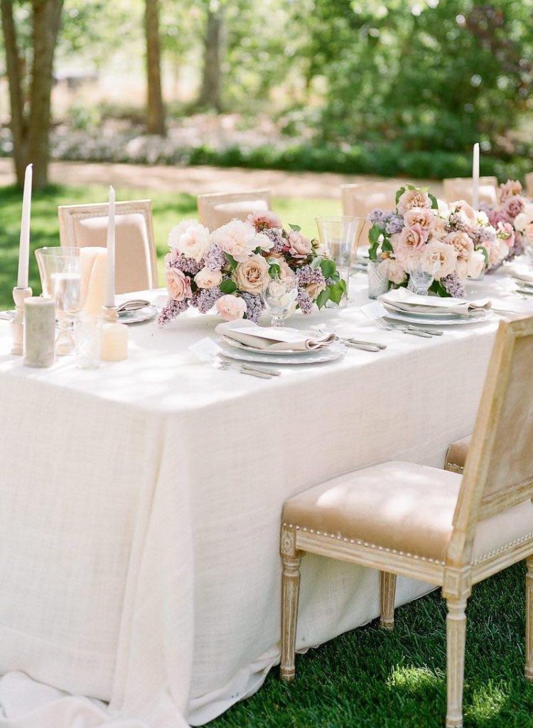 In questa foto un allestimento di nozze in stile classico con fiori lilla, rosa e bianco. Un tavolo imperiale è decoarato composizioni di fiori, sedie classiche e porcellane bianche