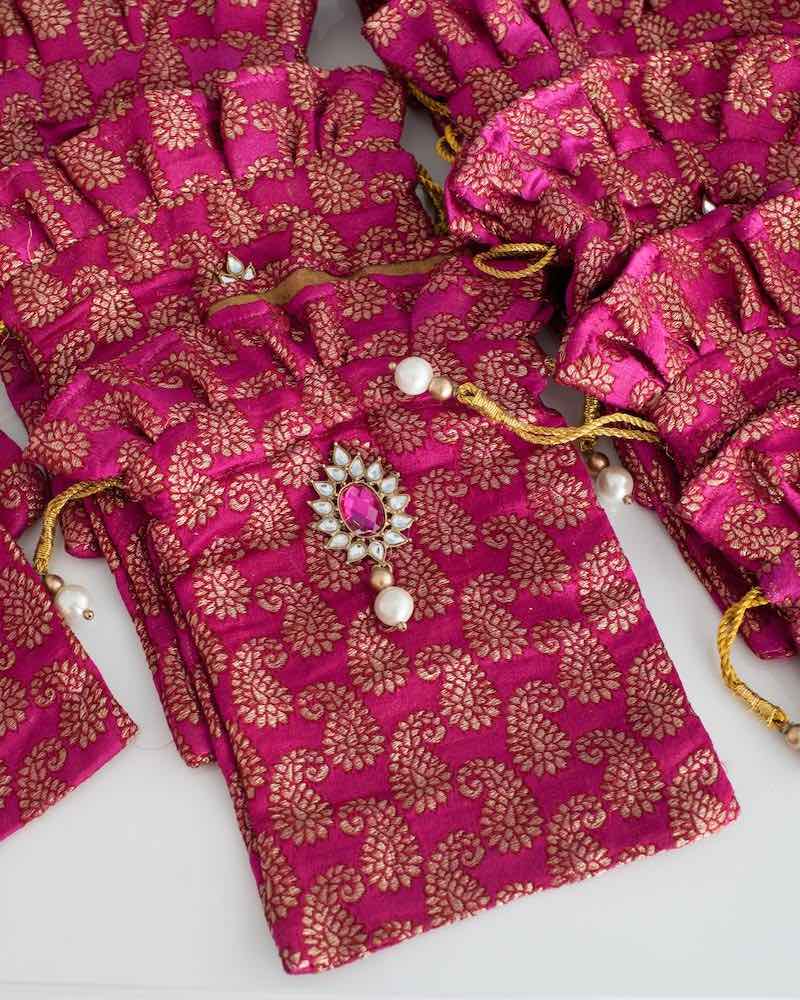 In questa foto sacchetti portaconfetti di seta di colore fucsia e oro con simboli orientali e applicazionie di cristalli e perle