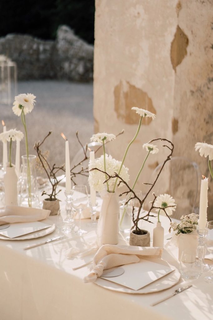 In questa foto un tavolo per matrimonio allestito in stile minimal con margherite di colore bianco, vasetti e tovaglioli abbinati