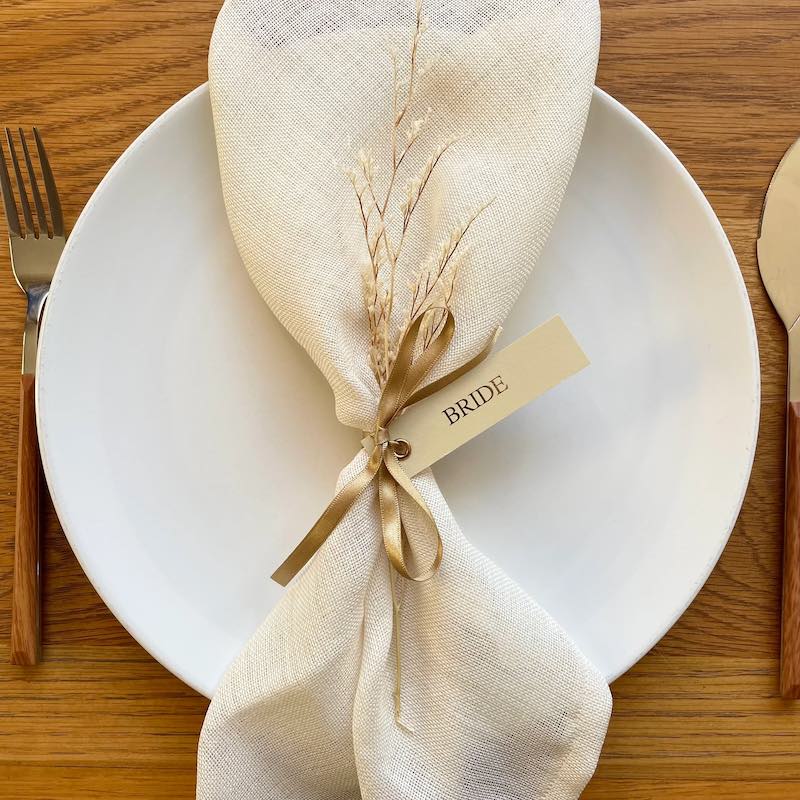 in questa foto un segnaposto per matrimonio in stile natural chic composto da fiori secchi di colore bianco e piccolo tag 