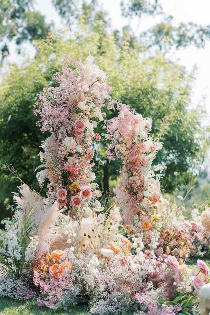 In questa foto un arco di fiori per un matrimonio romantico realizzato con rose di colore rosa, gypsophila di colore rosa, pampas