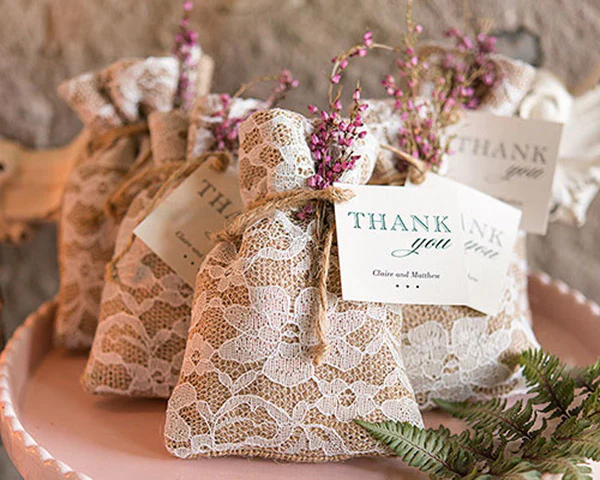 In questa foto sacchetti di pizzo bianco e iuta decorati con fiori secchi di colore fucsia usati come bomboniere di matrimonio shabby chic