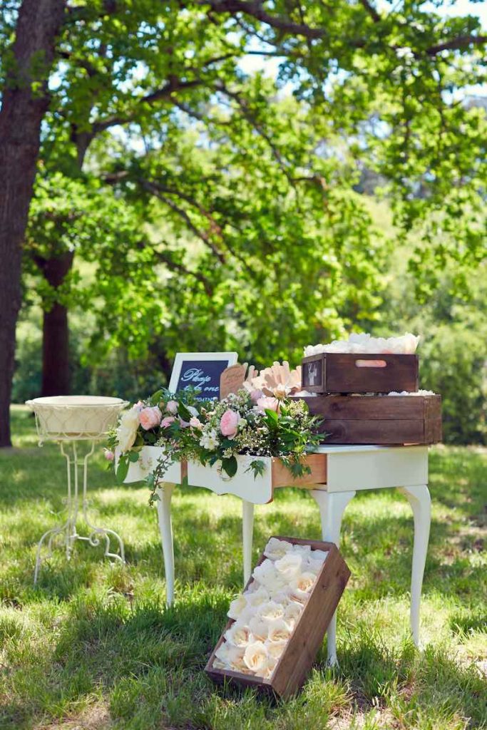 In questa foto decorazioni per un matrimonio in stile shabby chic con mobile antico di colore bianco decorato con rose di colore rosa e foglie e scatole di legno con conetti portariso