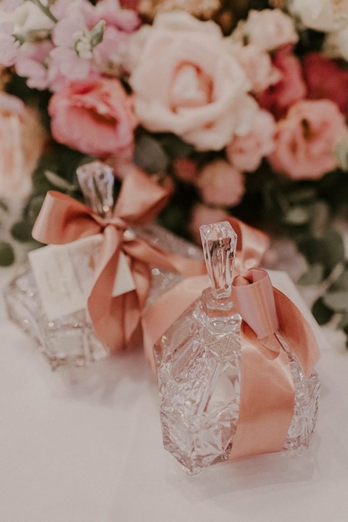 In questa foto due bottigliette di vetro decorate con un nastro rosa e posizionate davanti a fiori abbinate per un matrimonio vintage