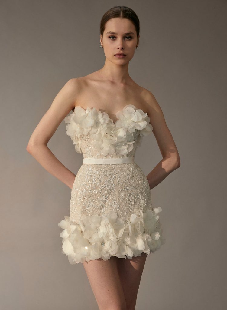 In questa foto una modella con un abito da sposa cortissimo, impreziosito dall'applicazione di fiori 3D, del brand Elie Saab per il 2023