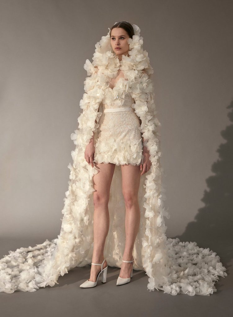 In questa foto una modella indossa un abito da sposa trasformabile 2023: minidress e mantella con cappuccio, della collezione bridal di Elie Saab 2023 