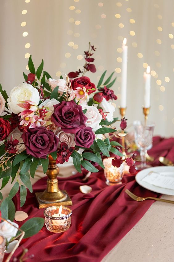 In questa foto una coppia di fiori posizionata su un drappo nel colore matrimonio 2023 Viva Magenta abbinato a posate di colore oro e fiori di colore bianco