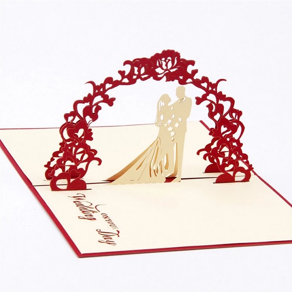 In questa foto, una partecipazione matrimonio pop up con al centro una coppia di sposi color crema sotto un arco di cuori rossi 