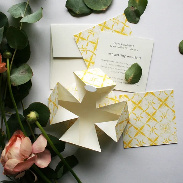 In questa foto, una partecipazione matrimonio origami beige con decori geometrici in giallo 