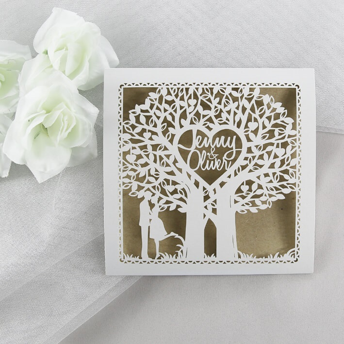 In questa foto, una partecipazione matrimonio fai da te con il disegno a rilievo in bianco di un albero con al centro un cuore con le iniziali degli sposi e sotto una coppia 