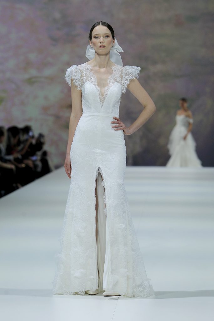 In questa foto la modella indossa un abito da sposa a sirena con spacco  e pizzo Marchesa for Pronovias 2023