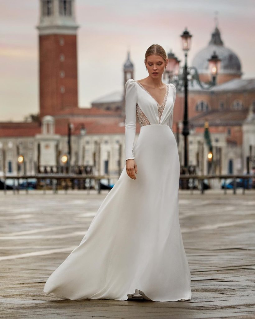 In questa foto la modella indossa un abito da sposa scivolato con scollo a V e maniche lunghe Nicole Milano