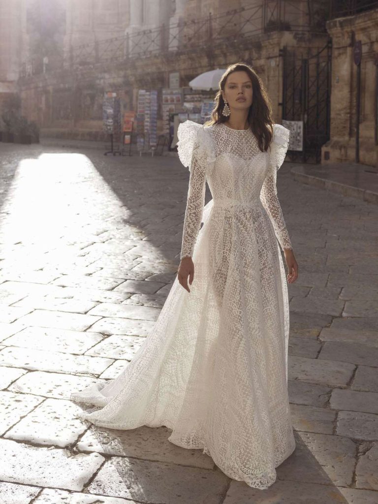 In questa foto la modella indossa un abito da sposa scivolato 2023 di pizzo con maniche lunghe Pinella Passaro