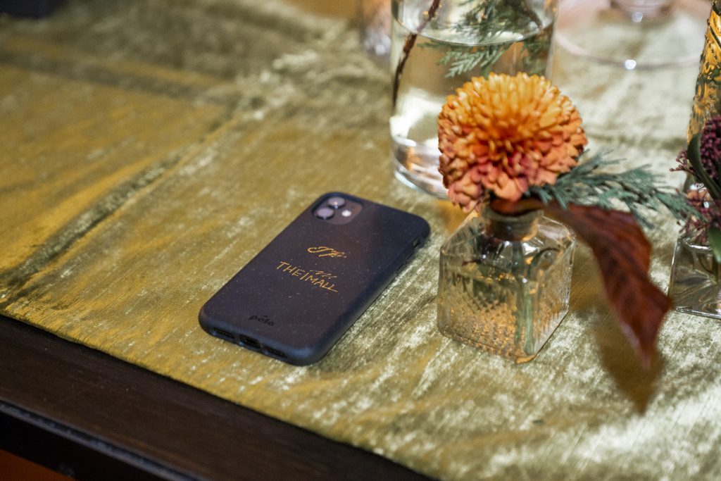 In questa foto, un cellulare poggiato su un tavolo allestito in occasione di Blossoms of Love 2022. La cover è blu e riporta la scritta The Mall in colore oro