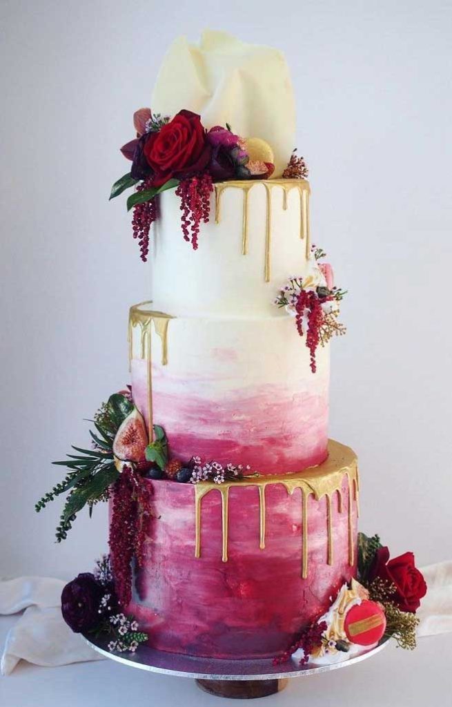 In questa foto una torta matrimonio a tre piani decorata con fiori e pennellate nel colore Viva Magenta e colate di colore oro