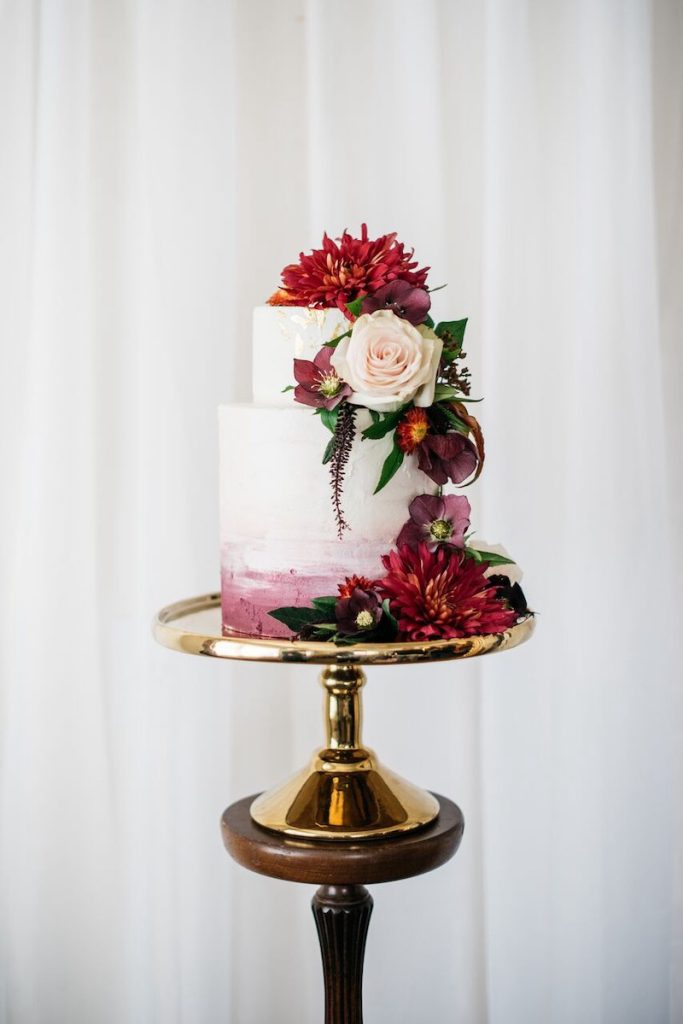 In questa foto una torta matrimonio a due piani posizionata su un piatto di colore dorato decorata con fiori e pennellate nel colore Viva Magenta