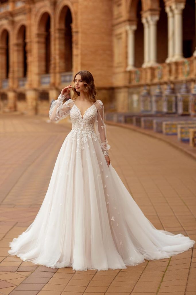 In questa foto una modella posa indossando un abito da sposa ampio di tulle con maniche a sbuffo lunghe e  fiori rame di Daniela Di Marino