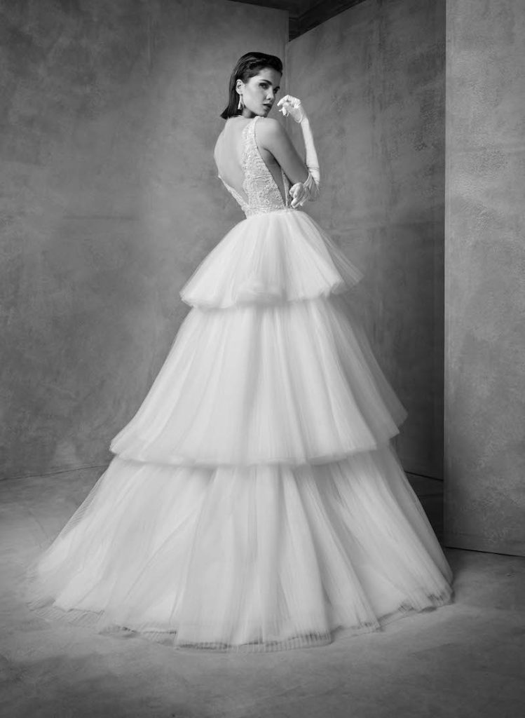 In questa foto una modella posa indossando un abito da sposa principessa con tulle a maxi balze e scollatura sulla chiena di Higar Novias