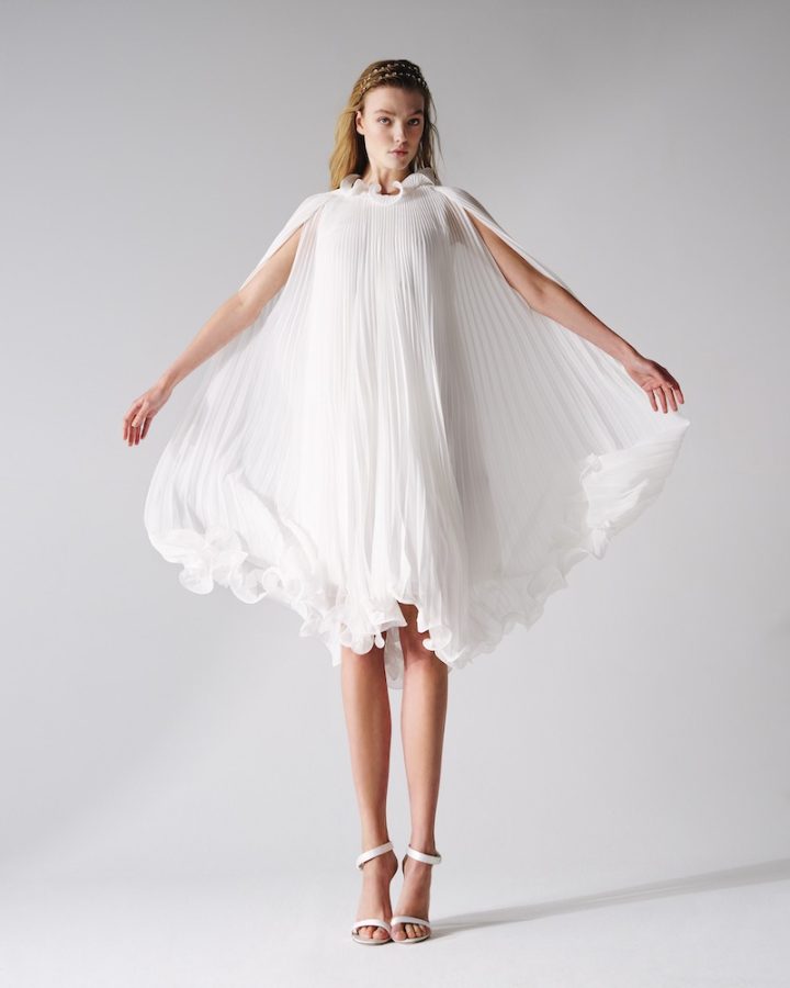 In questa foto una modella posa indossando un abito da sposa corto di Max Mara. L'abito è in seta plissettata e scollo all'americana 