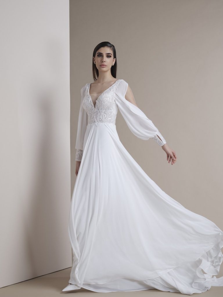 In questa foto una modella posa indossando un abito da sposa scivolato in chiffon di seta di Nadia Orlando con maniche a sbuffo e polsini