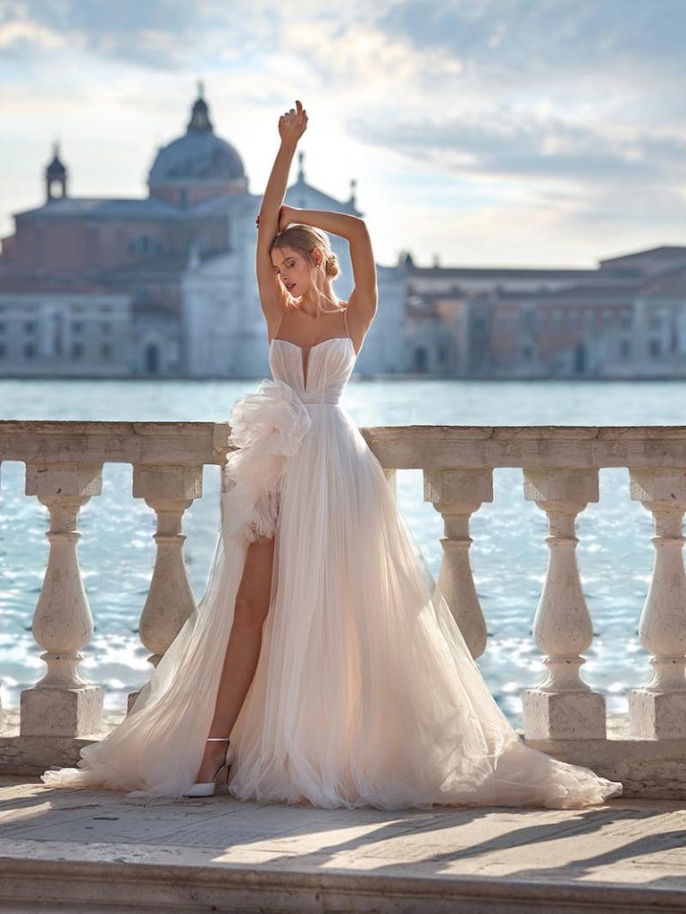 In questa foto una modella indossa un  modello di una delle marche di abiti da sposa italiani: Nicole Milano. L'abito è ampio in tulle con spacco e ruches su un fianco. Lo scollo è a V