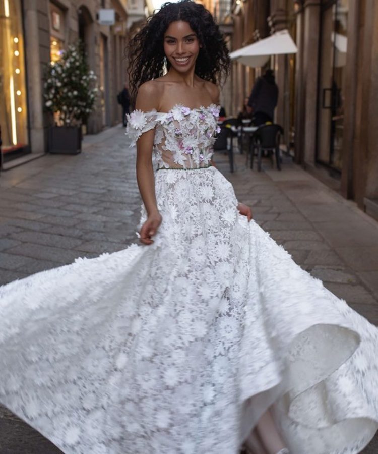 In questa foto una modella posa indossando un abito da sposa ad A in pizzo floreale e scollatura dritta di Rara Avis