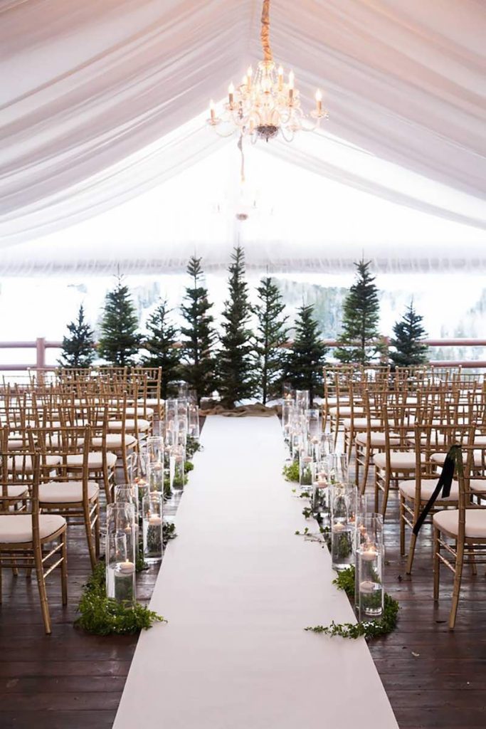 In questa foto una location per matrimonio a tema Natale: un tendono di colore bianco immerso in un bosco innevato con pini 