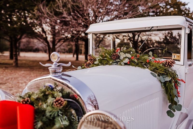 In questa foto un'auto per matrimonio  classica decorata con runner di foglie, bacche e pigne