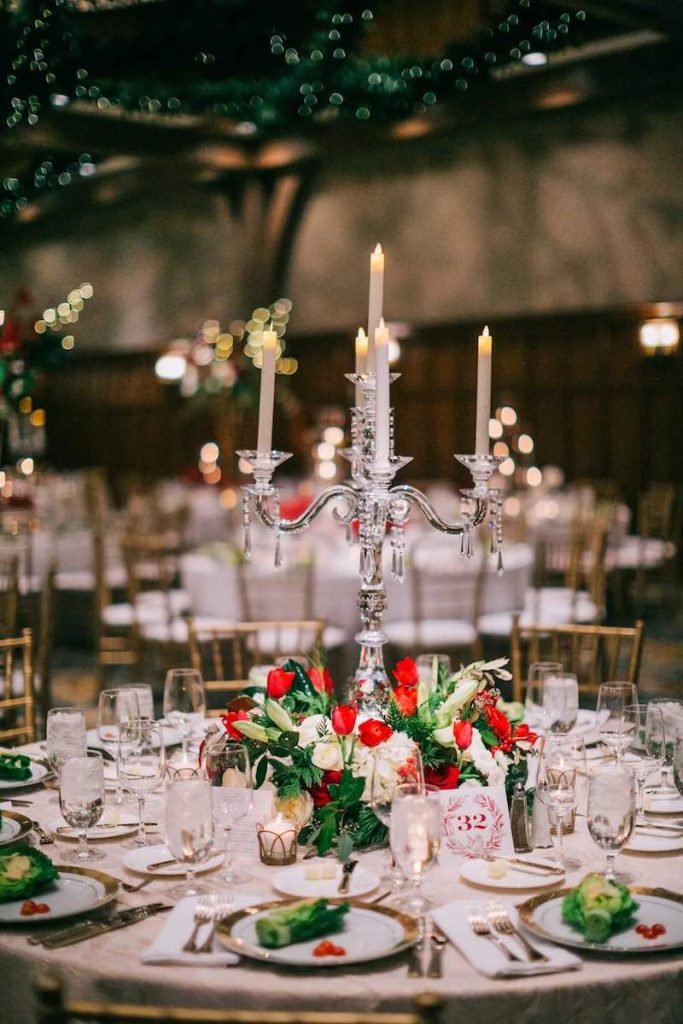 In questa foto un centrotavola composto da un candelabro di cristallo con candele di colore bianco decorato alla base con fiori di colore rosso e bianco