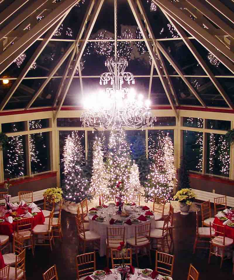 In questa foto una location per matrimonio a tema Natale: una serra decorata con alberi illuminati e tavoli rotondi allestiti con tovagliato di colore rosso e bianco