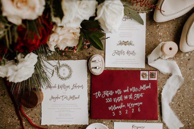 In questa foto inviti per matrimonio a tema Natale con busta di colore rosso, carta di colore bianco e testi di colore oro 