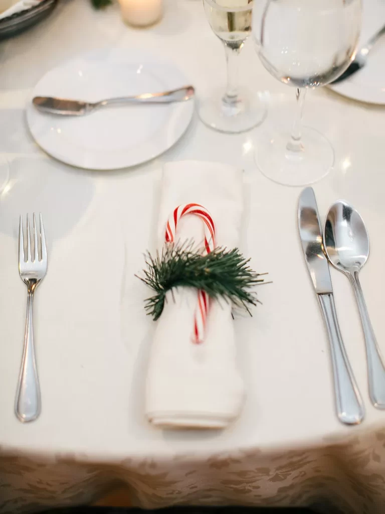 In questa foto un segnaposto per matrimonio a tema Natale a forma di bastoncino di zucchero fermato da un ramo di pino su un tovagliolo