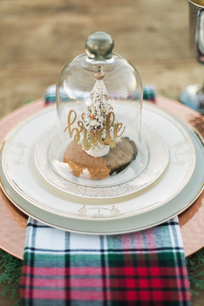In questa foto un segnaposto per matrimonio a tema Natale composto da una campana con il nome dell'ospite e, dentro, un piccolo alberello di colore bianco e oro