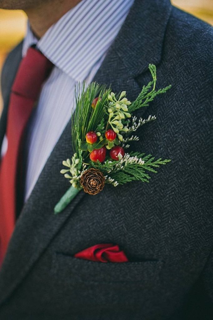 In questa foto il dettaglio di un fiore all'occhiello per lo sposo composto da aghi di pino, bacche di colore rosso e piccolo pigne