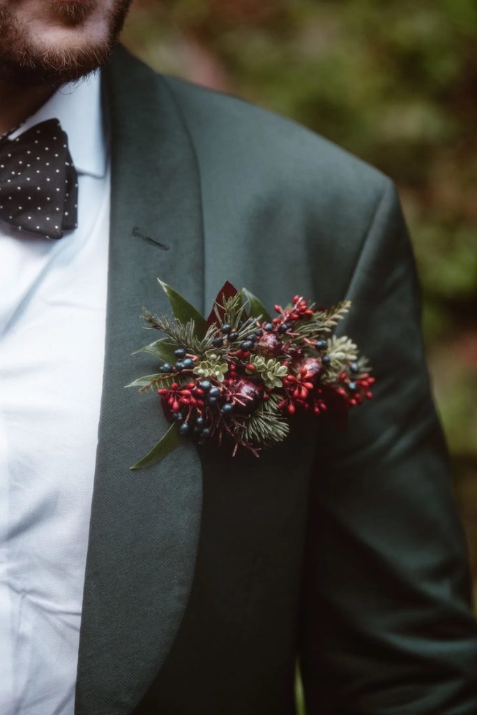 In questa foto il dettaglio di un fiore all'occhiello con aghi di pino e bacche di colore rosso