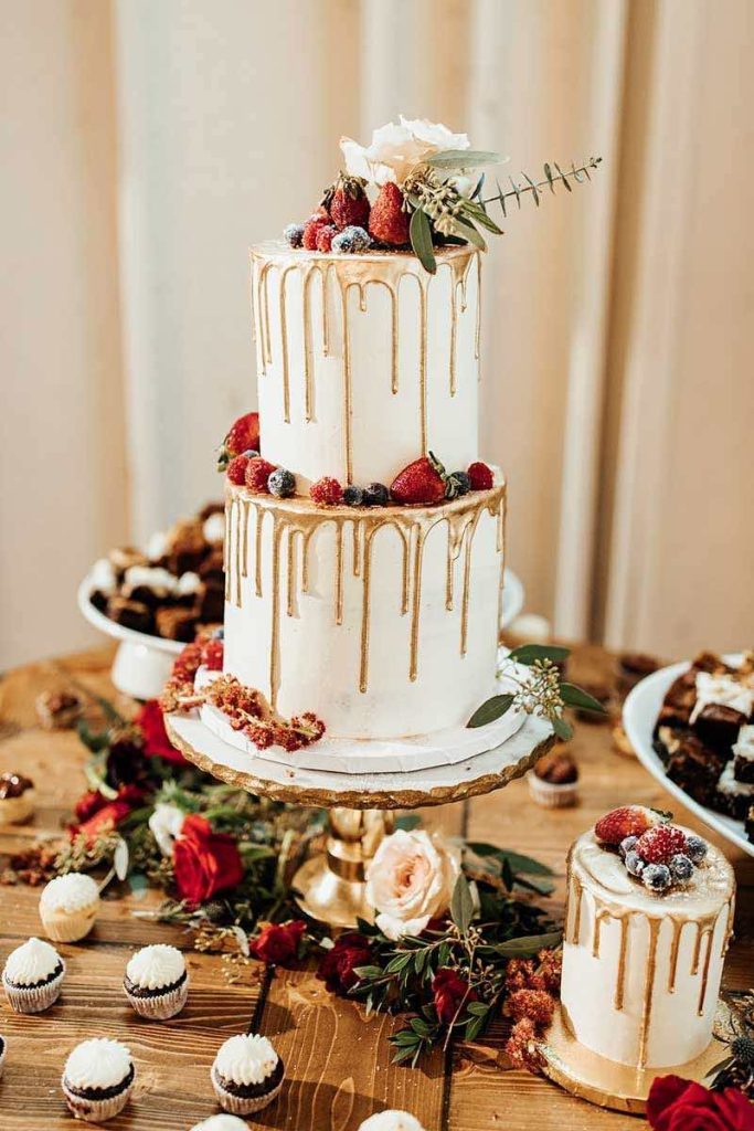 In questa foto una torta per matrimonio a tema Natale bianca con colate di colore oro decorata con frutti di bosco