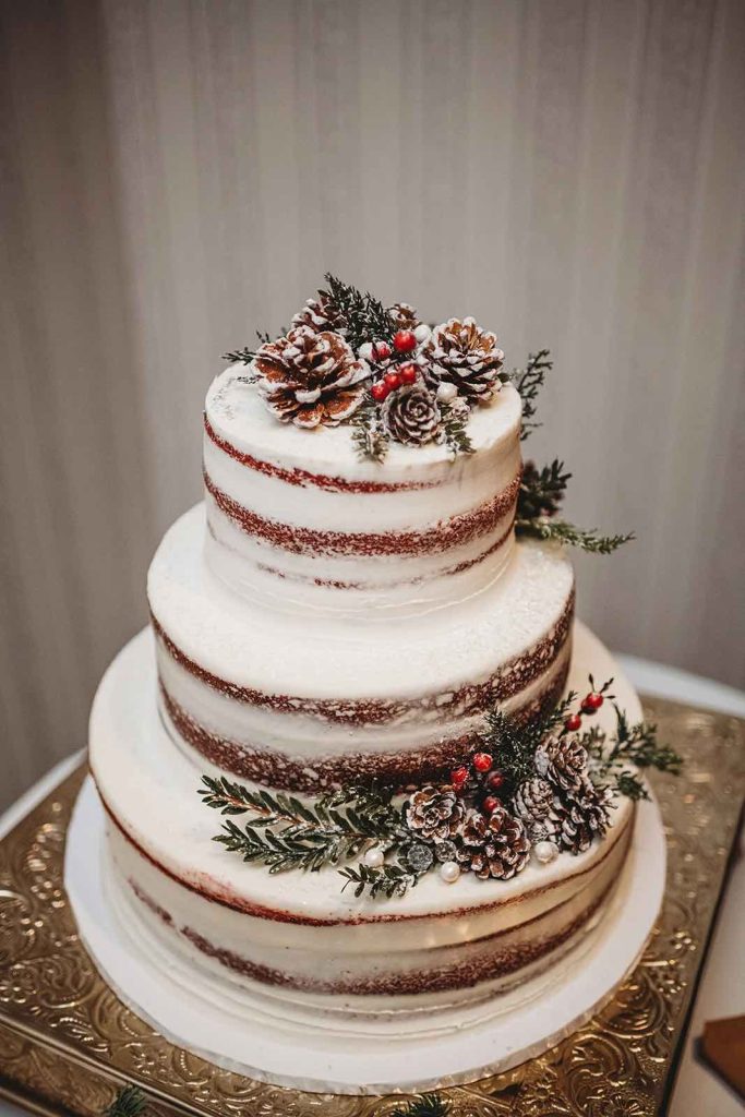 In questa foto una torta per matrimonio nake bianca decorata con pigne e rami di pino
