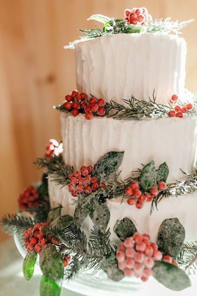 In questa foto una torta per matrimonio di colore bianco decorata con foglie verdi e bacche rosse