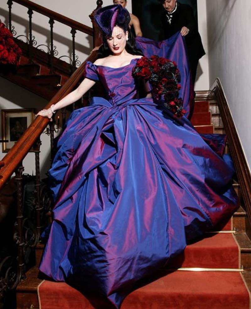 In questa foto Dita Von Teese scende le scale indossando l'abito da sposa viola disegnato per lei da Vivienne Westwood per il matrimonio con Marilyn Manson