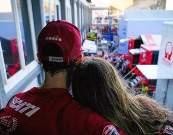 In foto Pecco Bagnaia, con la sua tuta da campione di Moto GP, e la fidanzata Domizia, abbracciati e di spalle.