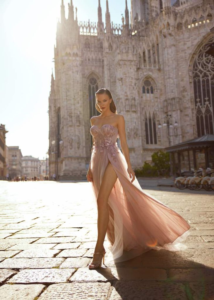 In questa foto una modella indossa un abito da sposa a sirena con spacco di colore rosa con spacco, scollo a cuore e dettagli 3D di Musani