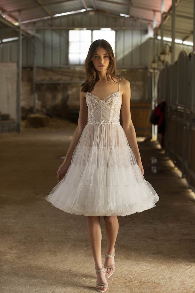 In questa foto una modella indossa un abito da sposa corto con balze in tulle  e piccolo fiocco di Berta