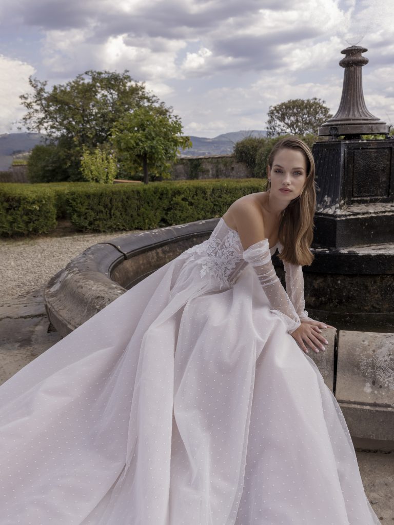 In questa foto la modella mostra le maniche dell'abito Ricca Sposa. in plumetis, sono lunghe e aderenti come un guanto e sono completamente indipendenti dal vestito da sposa