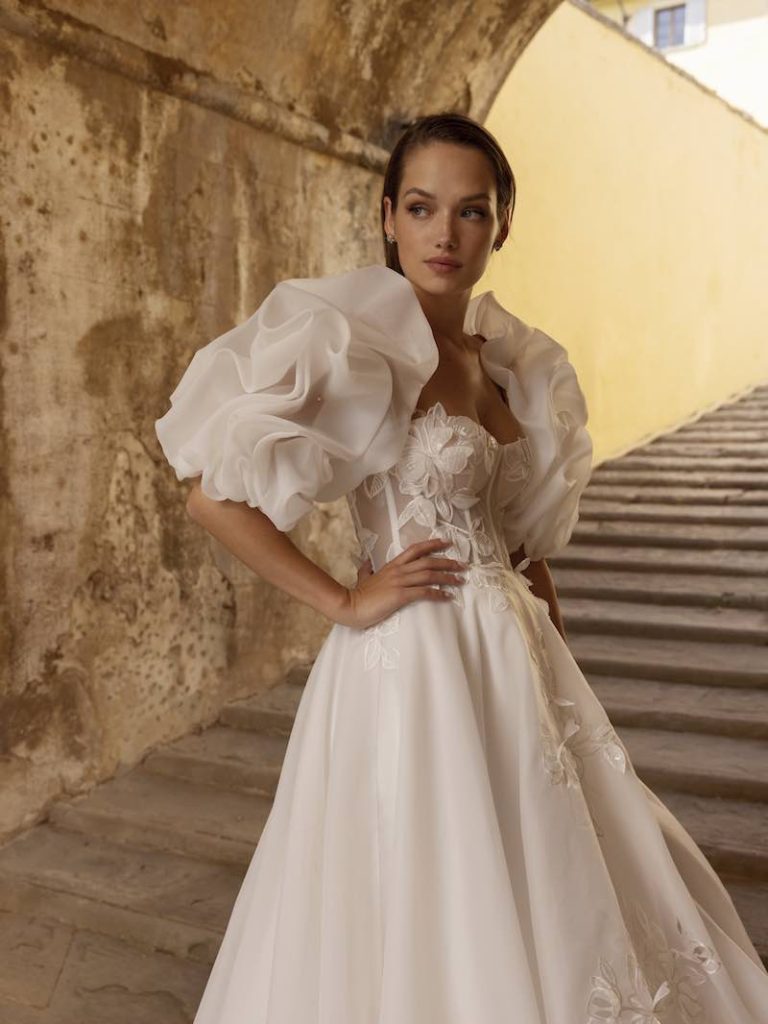 In questa foto una modella indossa un abito da sposa con maniche maxi realizzate in ruches